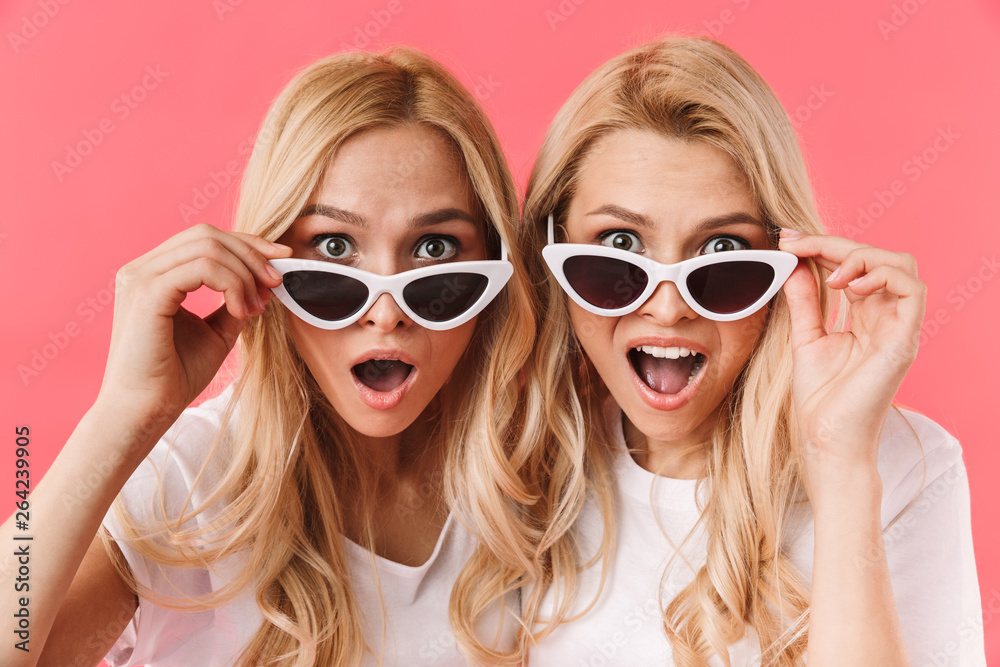 Shocked blonde twins take off sunglasses and looking at camera - obrazy, fototapety, plakaty 