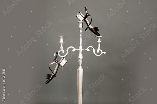 Vintage black beige sandals with rhinestones hanging from a silver candlestick on a gray background. Unusual fashion presentation photo