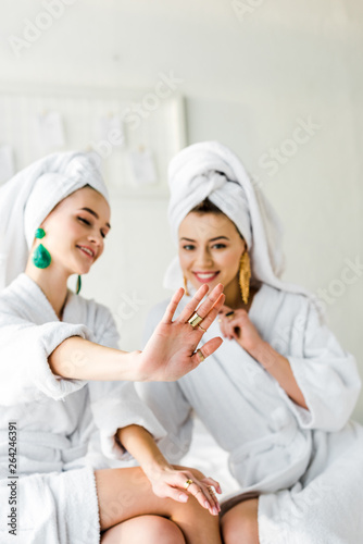 selective focus of stylish girls in bathrobes and towels on heads looking at rings on hand