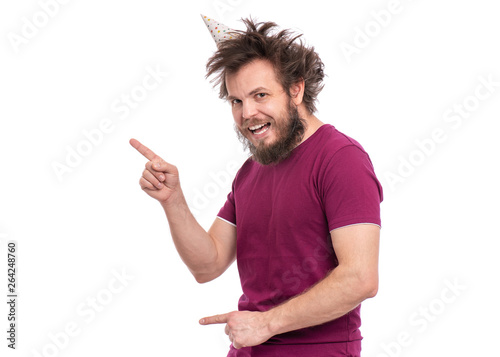 Crazy bearded Man with funny Haircut in birthday cap, isolated on white background. Happy guy smiling, looking at camera and showing something. Holidays, Emotions and Signs concept.