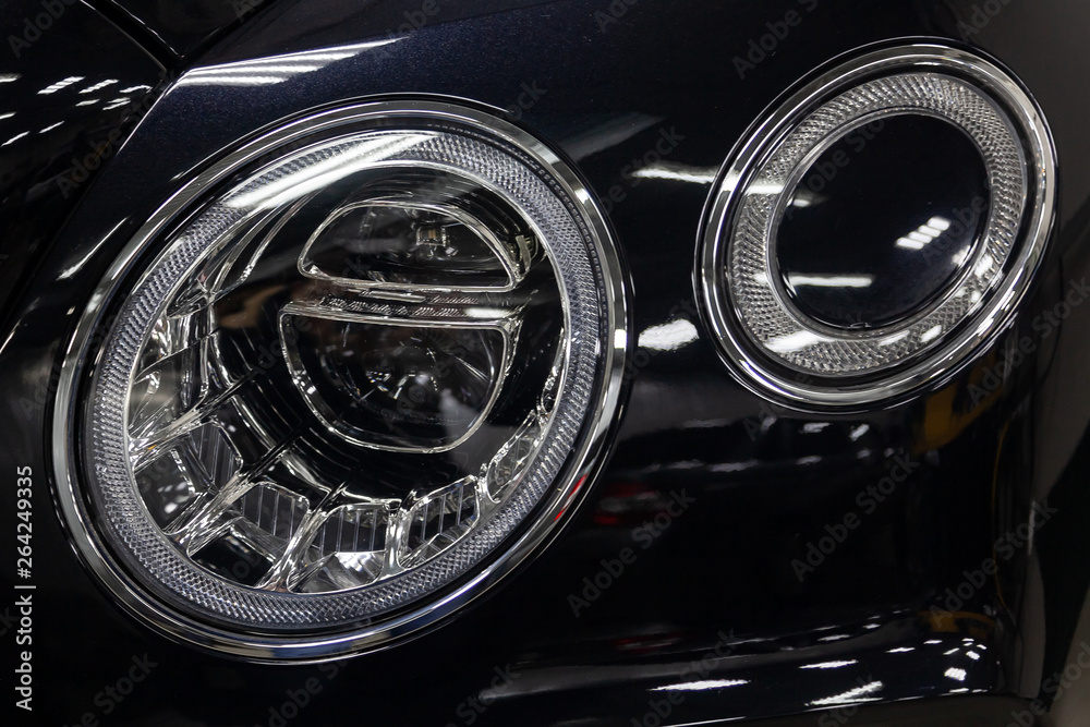 Front headlamp view of black used car stands in the auto showroom sale after washing and polish with led lens in auto service industry workshop