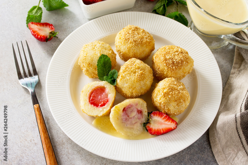 Cottage cheese dumplings with fresh strawberry, served with sour-honey sauce, delicious summer dessert on a bright stone table.