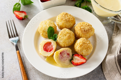 Cottage cheese dumplings with fresh strawberry, served with sour-honey sauce, delicious summer dessert on a bright stone table.