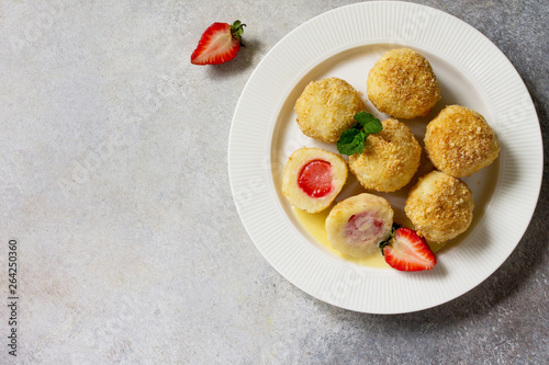 Cottage cheese dumplings with fresh strawberry, served with sour-honey sauce, delicious summer dessert on a bright stone table. Top view flat lay background, copy space.