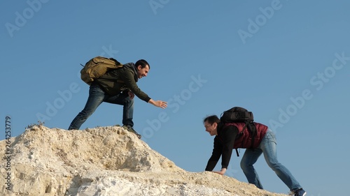 two climbers climb one after another on white rock. teamwork of business people. tourists give hand to each other  climbing to top of hill. team of male travelers goes to victory and success.