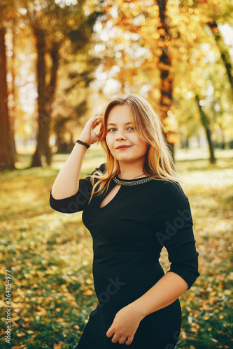 pretty cute girl with make up, dressed in black dress standing in a autumn park near trees