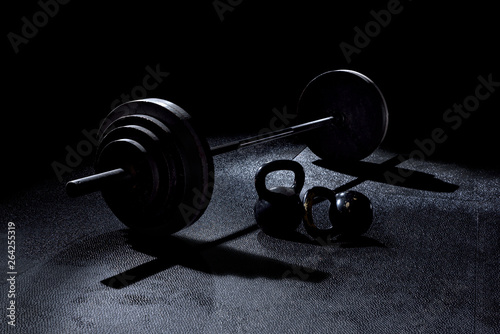 BACK LIT 365 pound weight on barbell with kettle bells on floor with dramatic light in gym