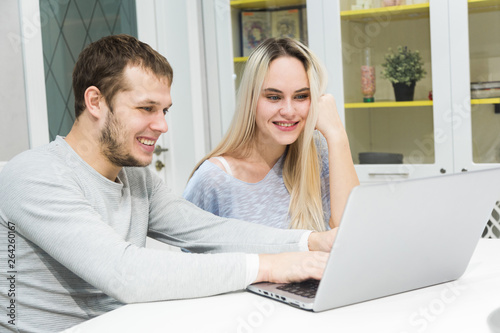 Young couple sitting at the morning in they kitchen and using laptop. Online shopping concept. Modern kitchen in background.