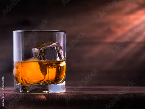 Glass of whiskey with ice cubes on the wooden table with wooden background