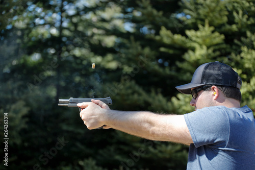 A man shooting a handgun with the ejected cartridge case in the air.