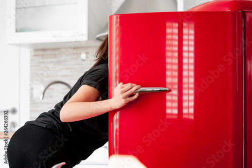 Woman looking for food in red refrigerator in modern bright apartments.