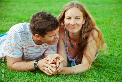 Beautiful woman laying on green grass with her husband. Happy couple.