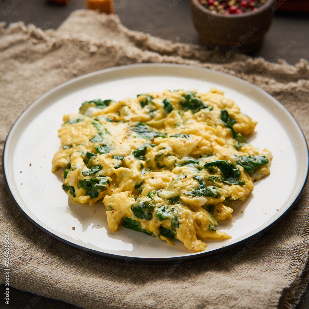 Scrambled eggs with spinach, cup of tea on dark brown background. Breakfast with Pan-fried omelette, side view Scrambled eggs with spinach, cup of tea on dark brown background. Breakfast with Pan-fried omelette, side view