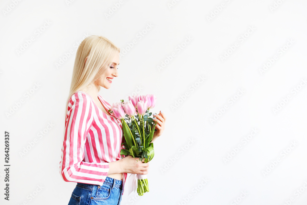 Studio portrait of gorgeous young blonde woman with long straight hair wearing pink stripe crop top shirt, holding bouquet of many tender pink tulips. White isolated background, copy space, close up. Studio portrait of gorgeous young blonde woman with long straight hair wearing pink stripe crop top shirt, holding bouquet of many tender pink tulips. White isolated background, copy space, close up.