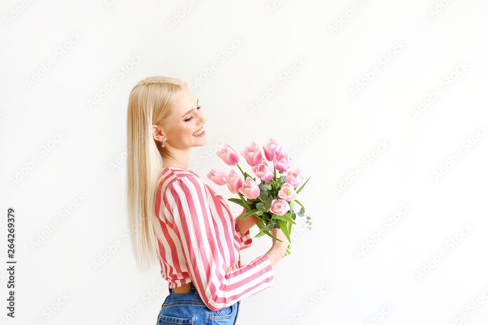 Studio portrait of gorgeous young blonde woman with long straight hair wearing pink stripe crop top shirt, holding bouquet of many tender pink tulips. White isolated background, copy space, close up. Studio portrait of gorgeous young blonde woman with long straight hair wearing pink stripe crop top shirt, holding bouquet of many tender pink tulips. White isolated background, copy space, close up.
