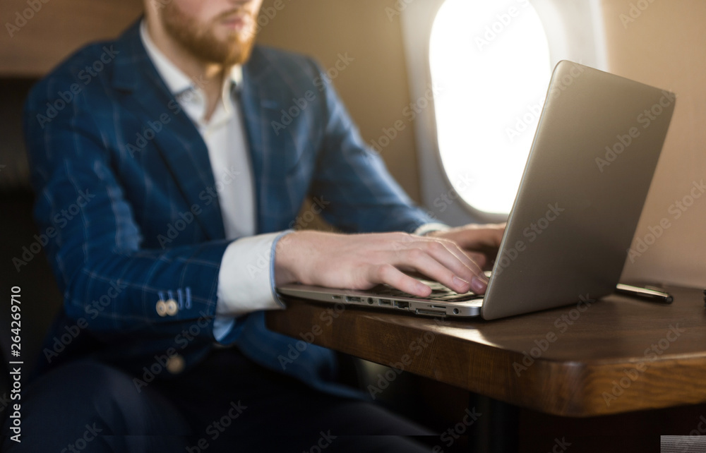 Attractive and successful businessman working on a laptop while sitting in a chair of his private jet. Attractive and successful businessman working on a laptop while sitting in a chair of his private jet.