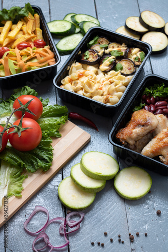ready meal to eat in lunch boxes, raw vegetables around, food containers on wooden table