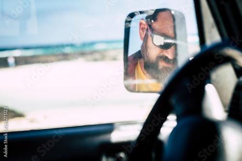 Caucasian man face with sunglasses viewed in the mirror of the car - alternative people portrait - travel vehicle concept