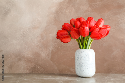 Vase with beautiful red tulips on table against brown background, space for text