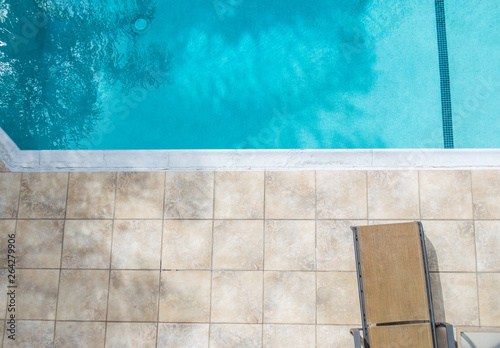empty lounger chair on a tile pool deck next to a clear blue swimming pool with copy space