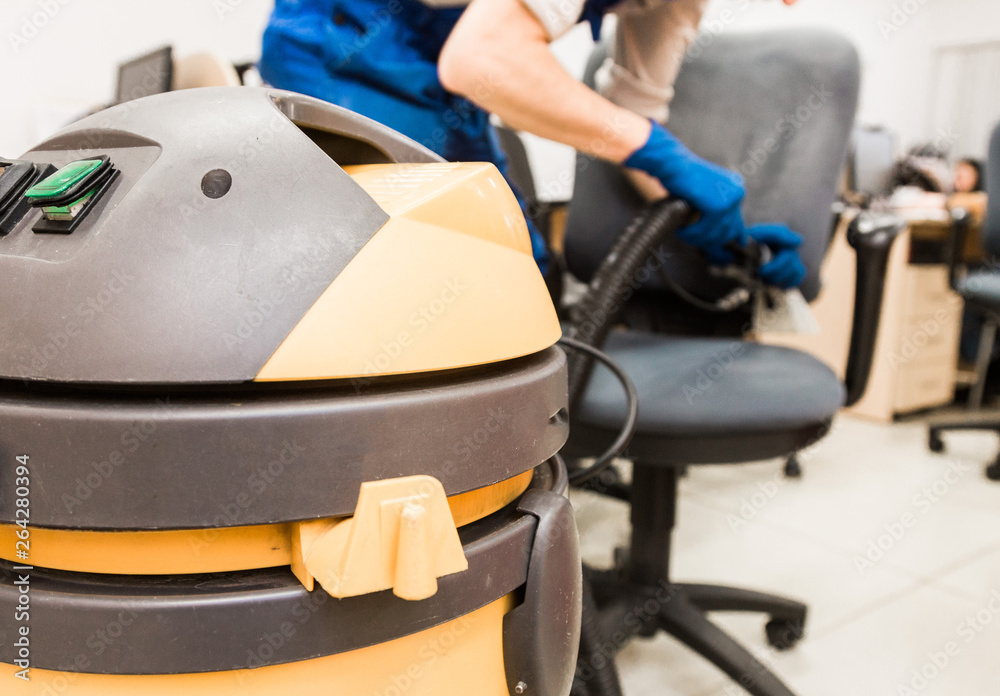 Young man in workwear and rubber gloves cleans the office chair with professional equipment. Young man in workwear and rubber gloves cleans the office chair with professional equipment.