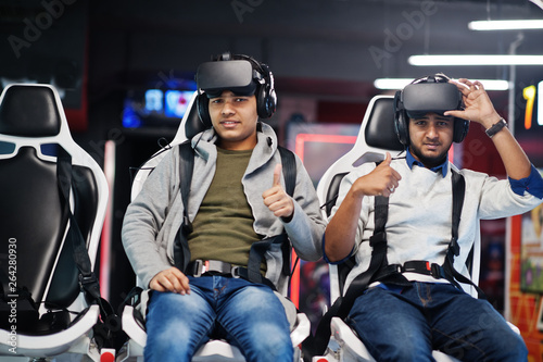 Two young indian people having fun with a new technology of a vr headset at virtual reality simulator. They happy and show thumb up.