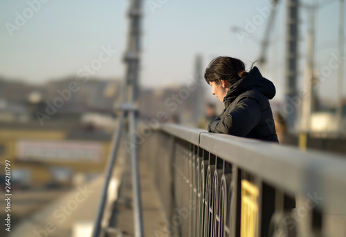 Lonely young brunette girl stands on the bridge on a sunny day