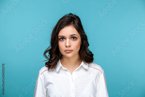 Closeup portrait of brunette beautiful girl in a white blouse isolated over the blue background