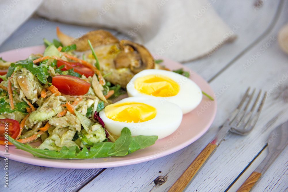 The concept of proper nutrition, keto diet, paleo diet. Salad with fresh vegetables and avocado, baked chicken breast with mushrooms and boiled egg on a pink plate, next to cutlery