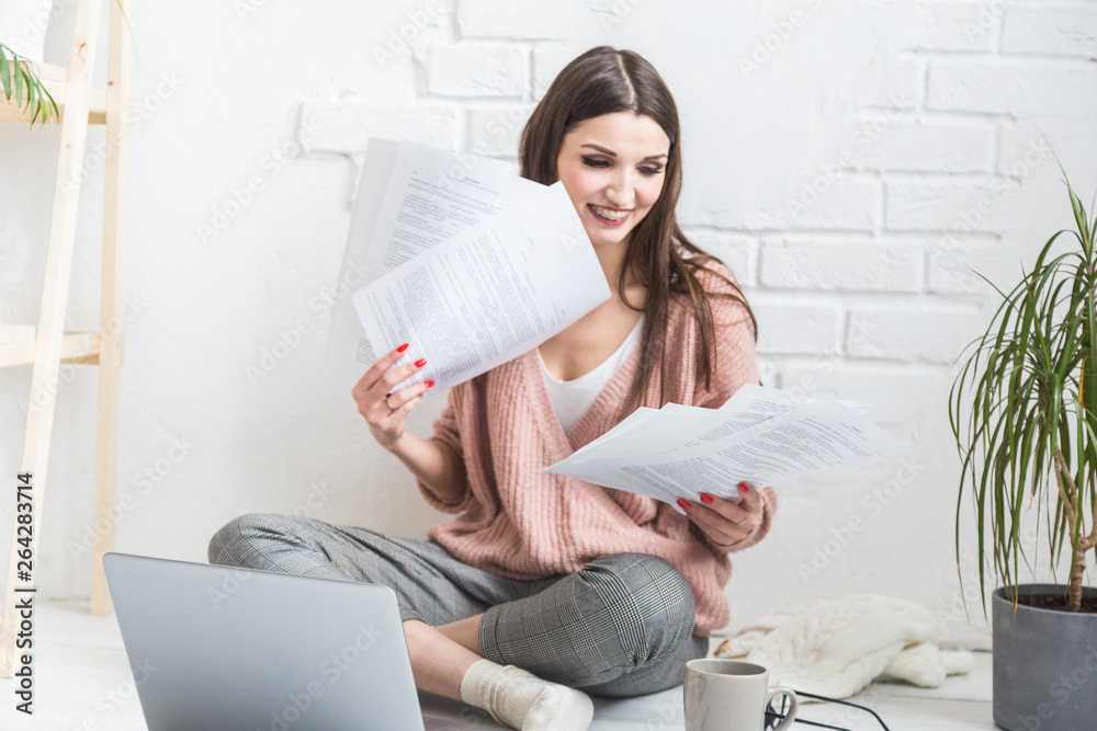 Happy woman examines the paper sitting near the laptop, the girl freelancer works with documents. Student female gets education remotely online Happy woman examines the paper sitting near the laptop, the girl freelancer works with documents. Student female gets education remotely online