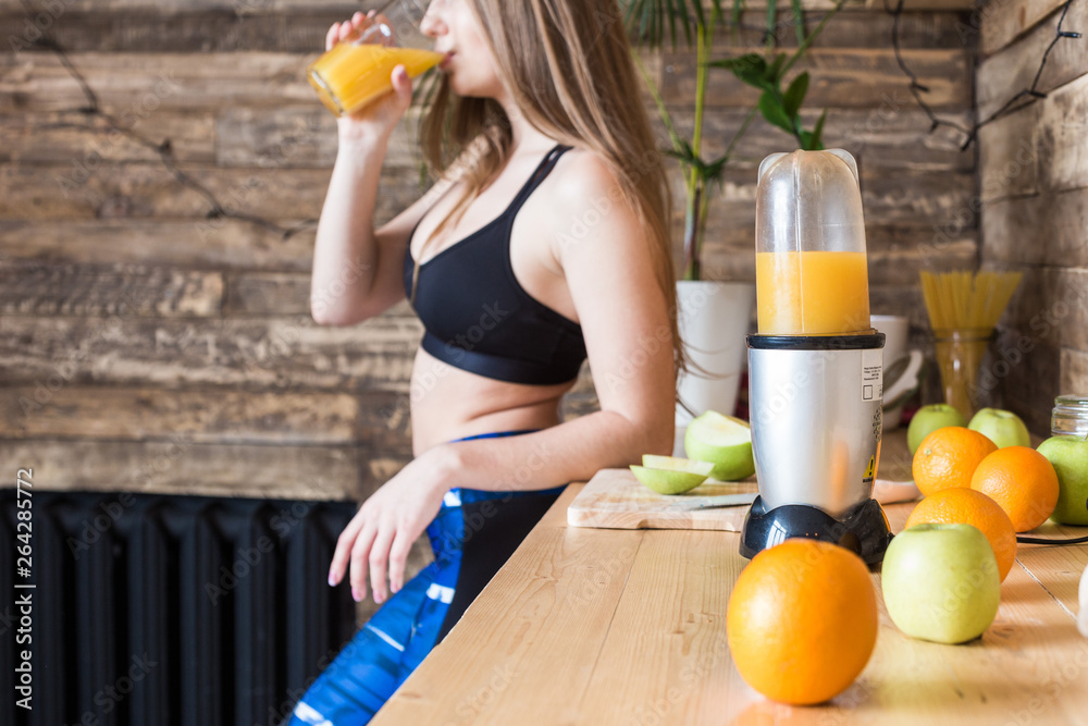 Attractive girl in sportswear prepares a healthy breakfast before the workout in the kitchen, cuts fruit and drinks fresh juice made in a juicer. The benefits of healthy eating, fitness and beauty Attractive girl in sportswear prepares a healthy breakfast before the workout in the kitchen, cuts fruit and drinks fresh juice made in a juicer. The benefits of healthy eating, fitness and beauty