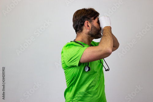 Portrait of male veterinary doctor in green uniform with brown hair pretending to use binoculars, facing forwards and looking at the side. Isolated on white background.