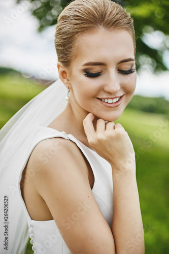 Beautiful blonde model woman with closed eyes and with elegant wedding hairstyle smiling and posing outdoors