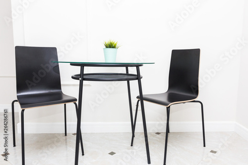 A glass table and black chairs in the Scandinavian style in the interior of a bright modern apartment. Kitchen area