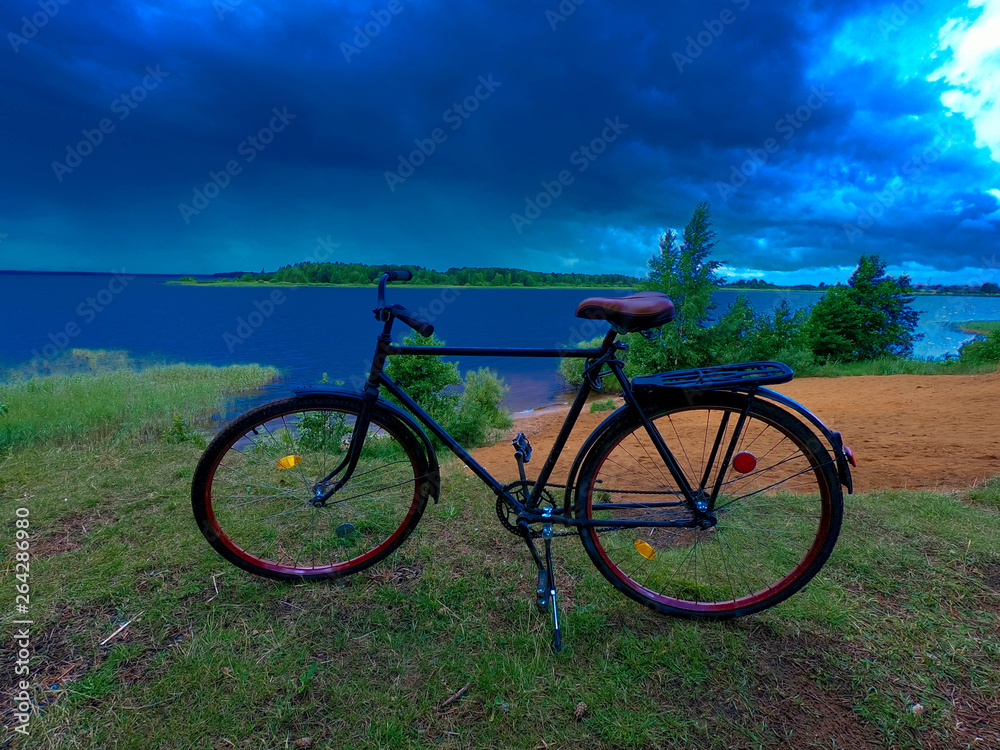 Fototapeta premium Adult road bike on the bank of a cloudy river.