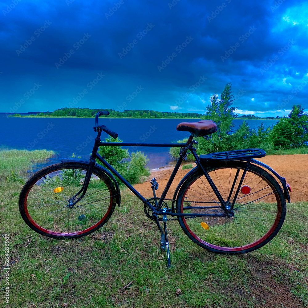 Fototapeta premium Adult road bike on the bank of a cloudy river.