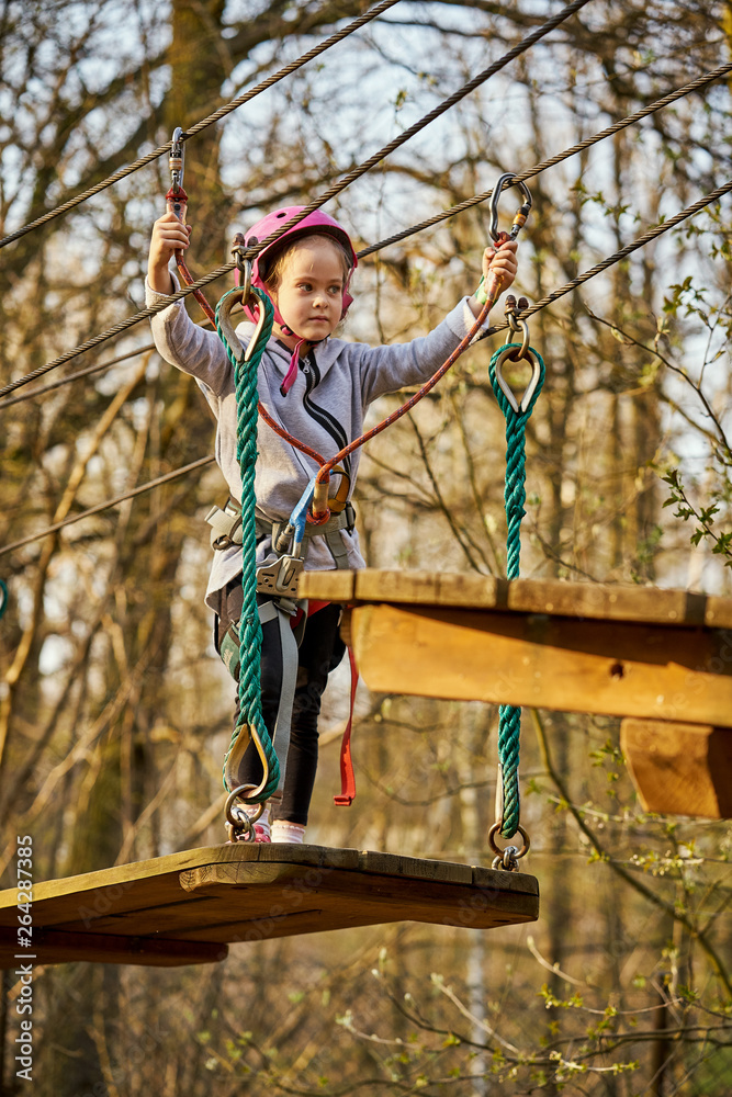 Adorable little girl in helmet in rope park in forest