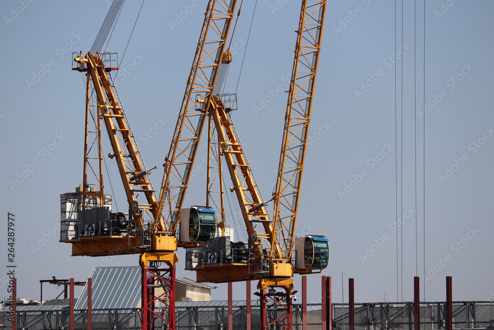 Two construction cranes and unfinished building on background of clear blue sky. Concept of heavy lifting or cargo port