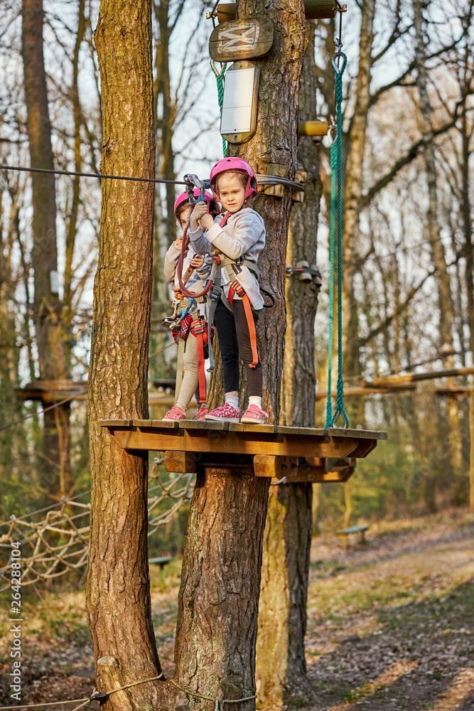 Two adorable little girls in helmet in a rope park in the woods Two adorable little girls in helmet in a rope park in the woods