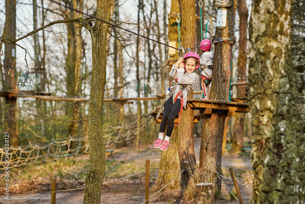 Two adorable little girls in helmet in a rope park in the woods