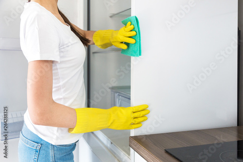 A young woman from a professional cleaning company cleans up at home. A man washes the kitchen washes the fridge in yellow gloves with cleaning supplies stuff.