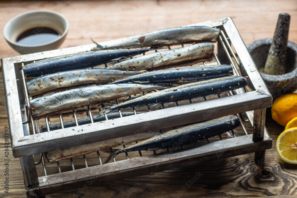 Raw saury on a grill for smoking with lemon and herbs top view