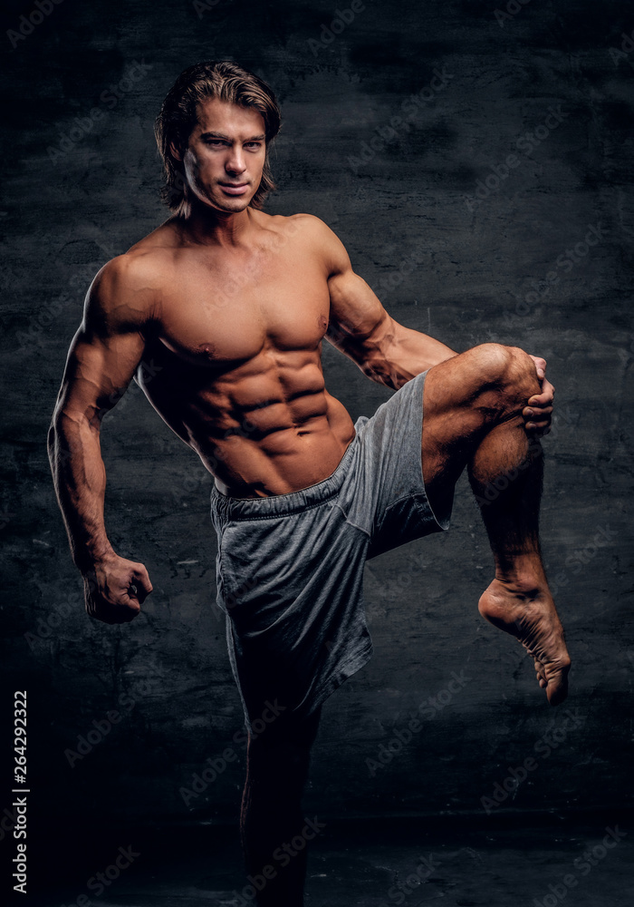 Smiling attractive bodybuilder with naked torso is doing leg
