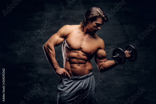 Attractive muscular man is posing with dumbbell. He has naked torso.