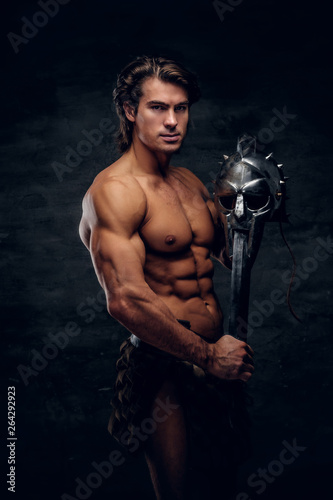 Manly athlete with sword and helmet in his hands. He is wearing gladiator s bandage.