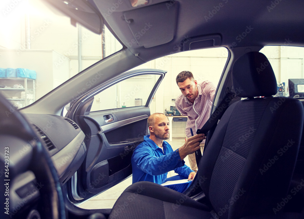 auto service, repair, maintenance and people concept - mechanic checking car seat belt with man or owner at workshop