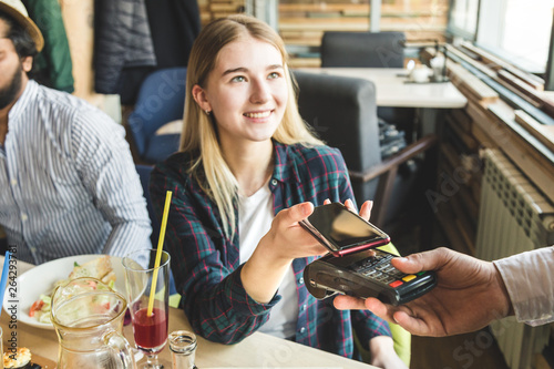 Young attractive woman paying in cafe with contactless smartphone payment