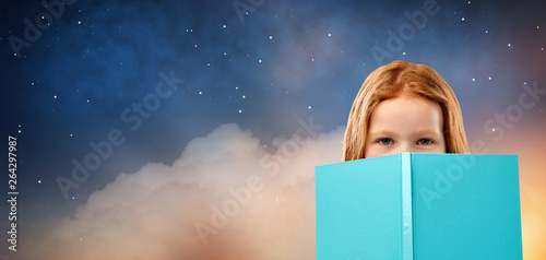 reading, childhood and people concept - red haired girl hiding behind book over starry night sky background © Syda Productions