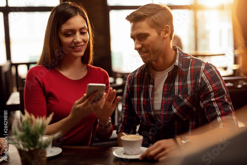 Happy couple using mobile phone together in a cafe,