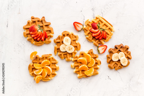 Homemade Viennese waffles with strawberry, tangerine and banana topings on white background top view